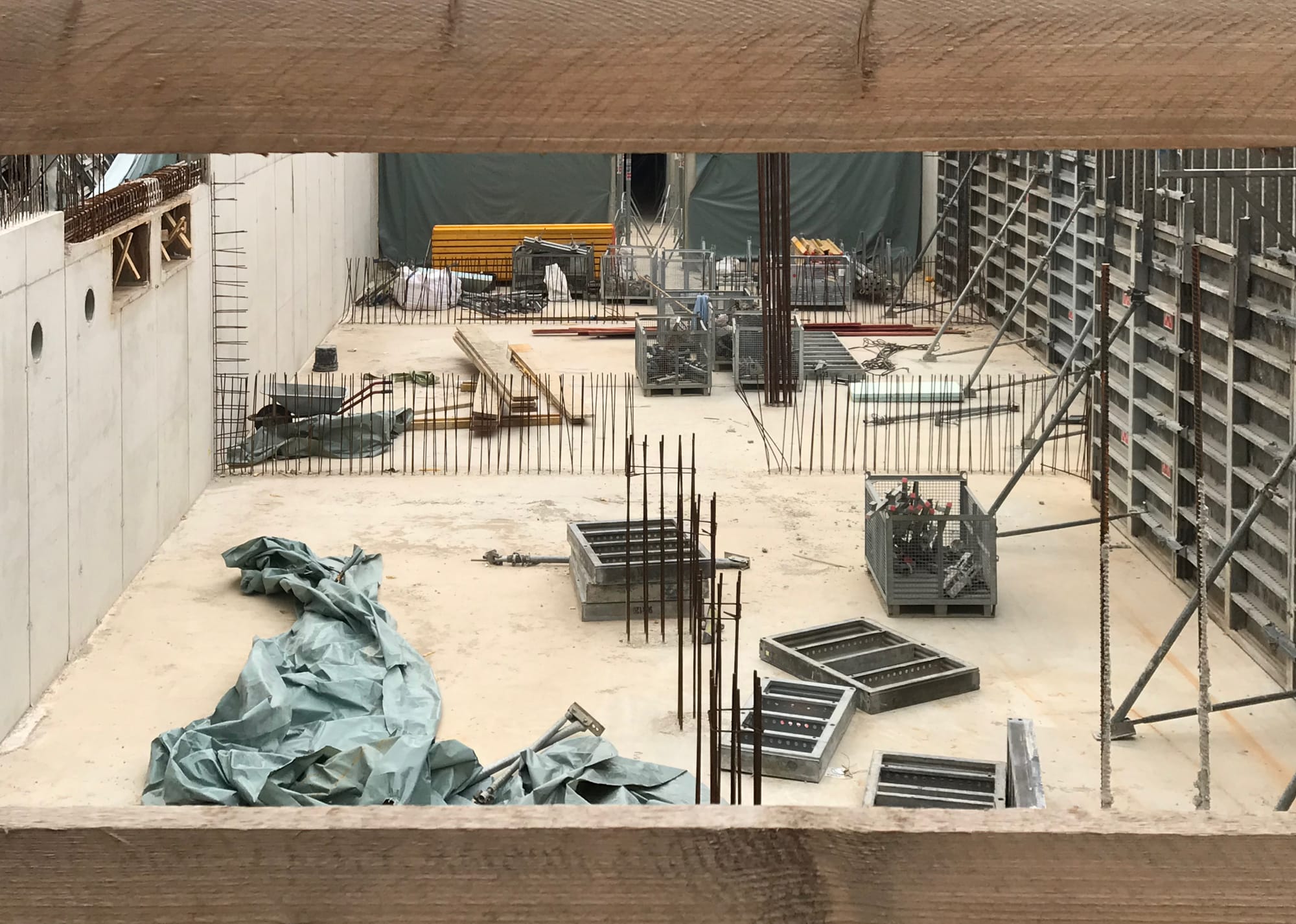 Baustelle durch Bauzaun fotografiert wie eine Bühnenkulisse: Wände Stahlstäbe Betonwand wie Kunstwerke verteilt auf dem Grundbeton